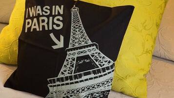 Almohada negra con una Torre Eiffel blanca y texto sobre un sofá color beige.