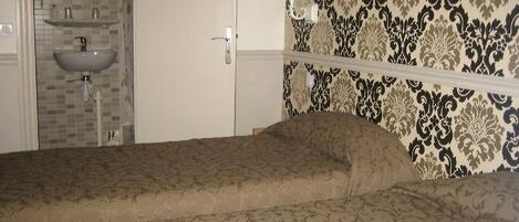 A bedroom with a bed, a white wardrobe, a bathroom with a sink and mirror, and patterned wallpaper.