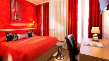 Una habitación de hotel con cama, escritorio, silla, televisor y ventana con cortinas.
