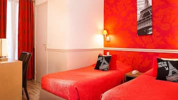 Habitación de hotel con dos camas, un escritorio y una silla. Hay una lámpara de pared y un cuadro con la Torre Eiffel.
