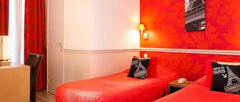 A hotel room with two beds, a desk, and a chair. There is a wall-mounted lamp and a framed picture of the Eiffel Tower.