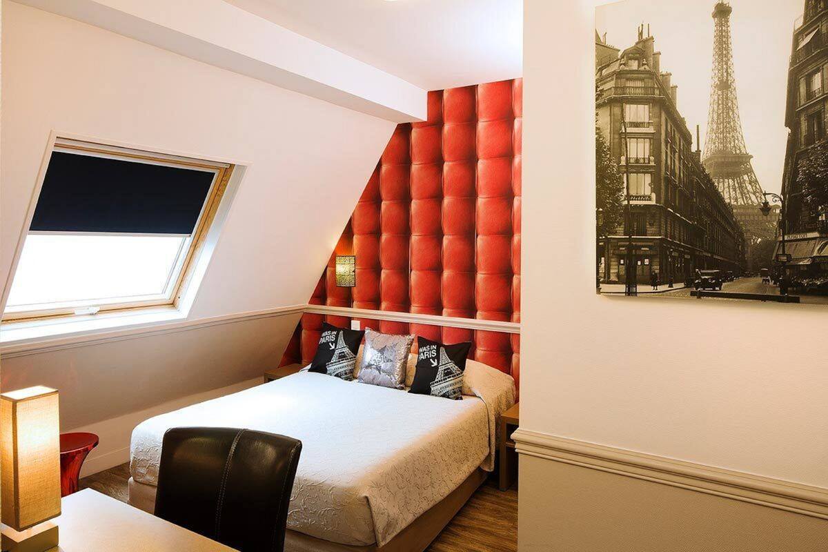 A bedroom with a bed, a red upholstered headboard, a window with a blind, and a poster of the Eiffel Tower.