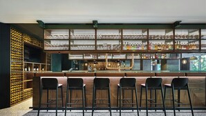 A bar area with wooden bar counters, black bar stools, and shelves of bottles and glasses. - Four Points by Sheraton Wroclaw (Wroclaw)