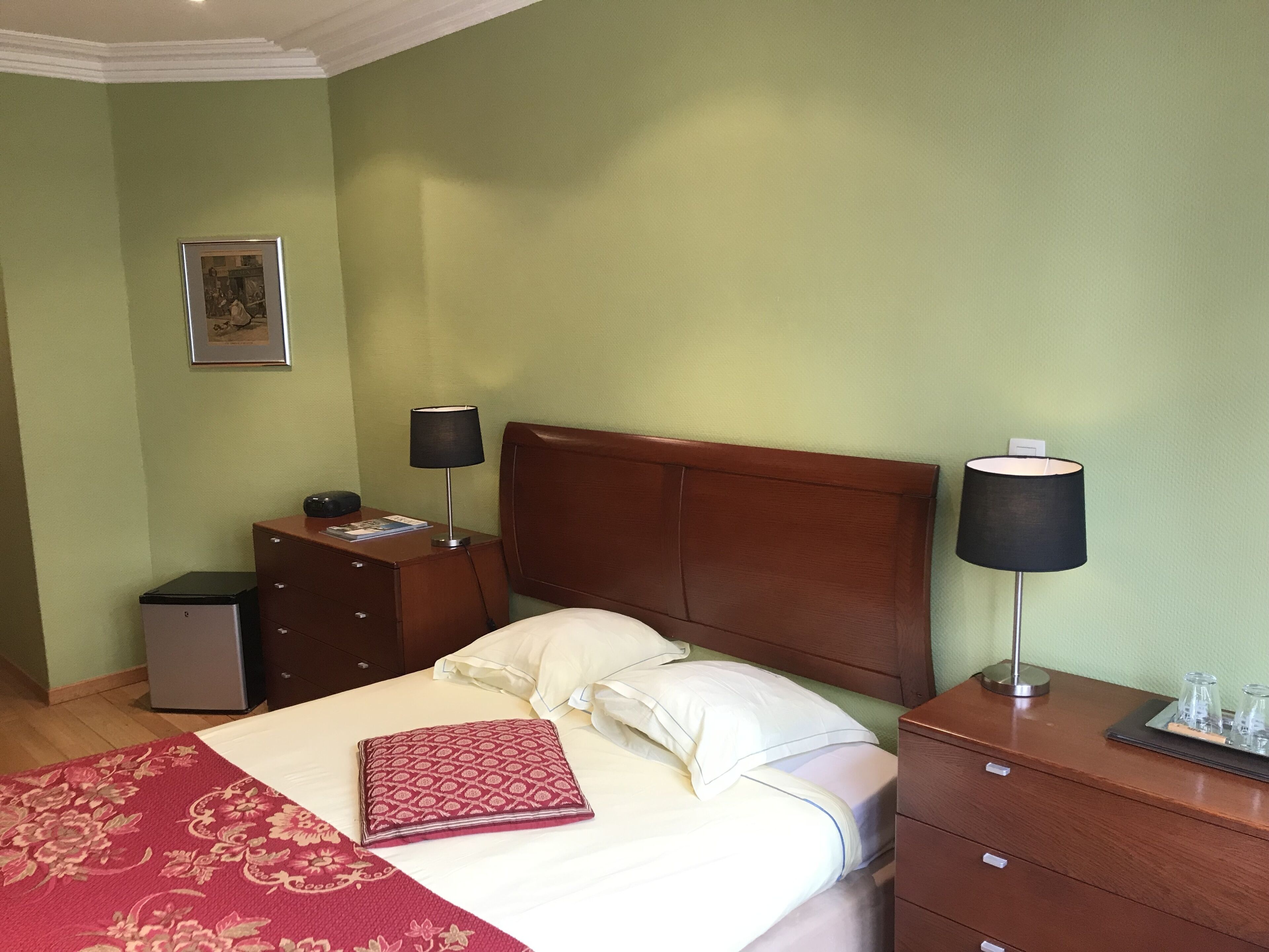 Een keurig opgeruimde hotelkamer met een bed, nachtkastjes, een bureau en een klein kastje.