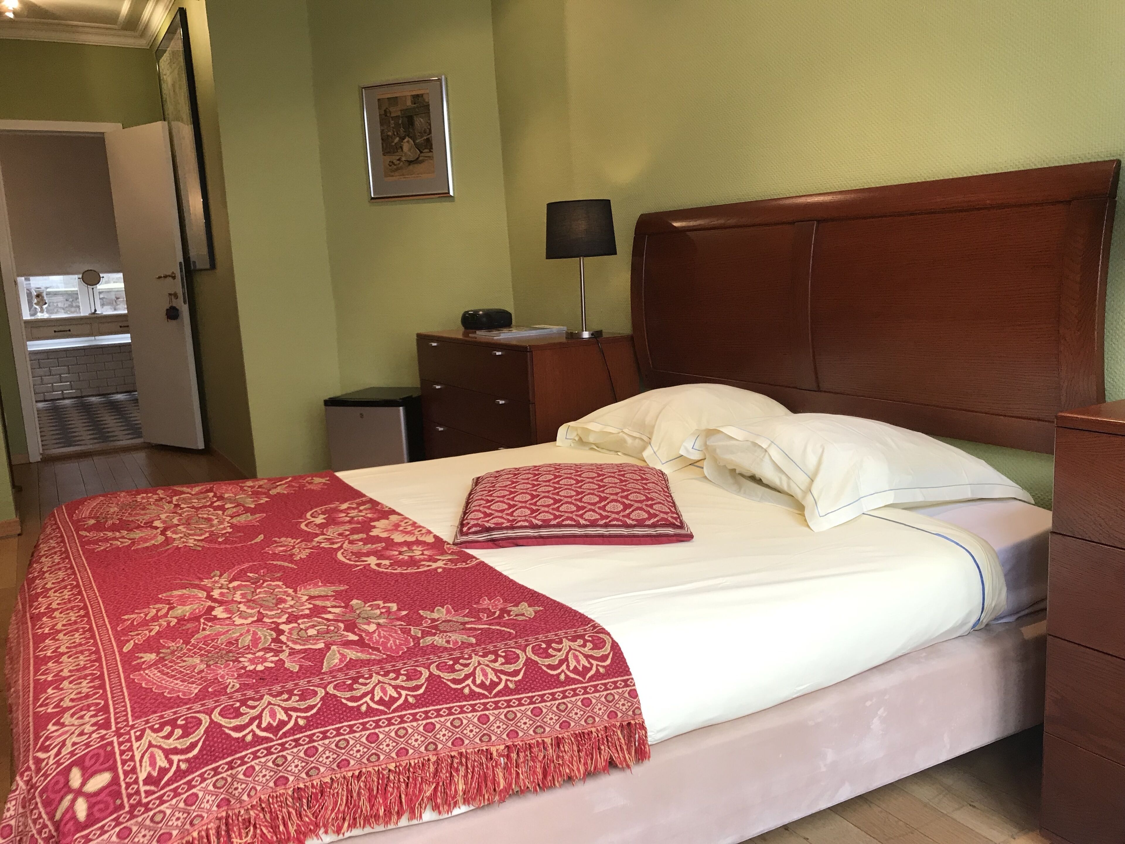 A neatly made bed with a red and white patterned bedspread, a wooden headboard, and a small bedside table with a lamp.
