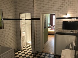 Une salle de bain avec des carreaux de céramique blancs rectangulaires, un carrelage à motifs à carreaux, une baignoire, des toilettes et un espace douche.