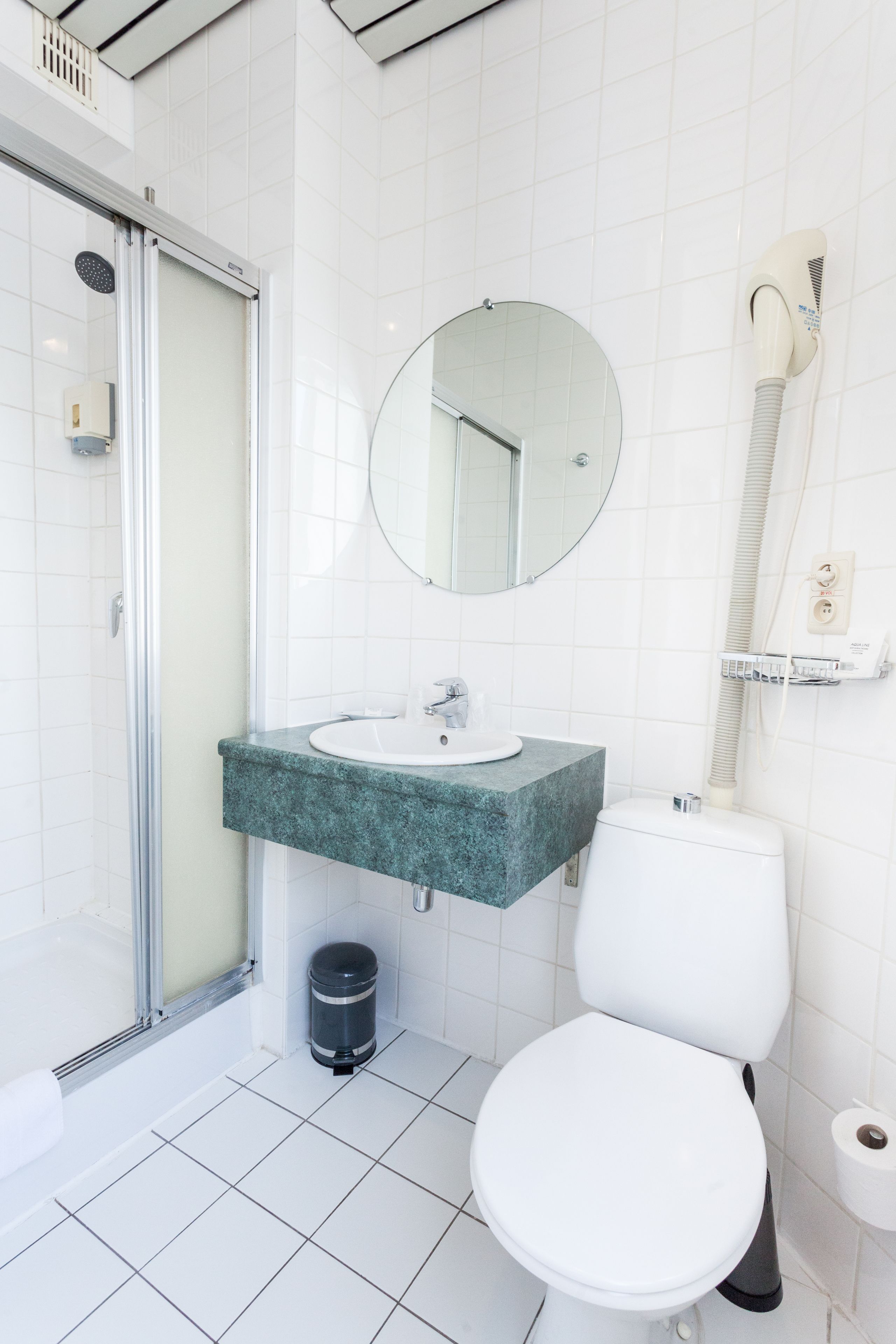 Et badeværelse med brusekabine i glas, vask med spejl og toilet.