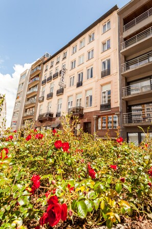 A multi-story hotel with balconies, a garden with red roses, and a clear blue sky. - Malecot Hotel by F-Hotels (Blankenberge)