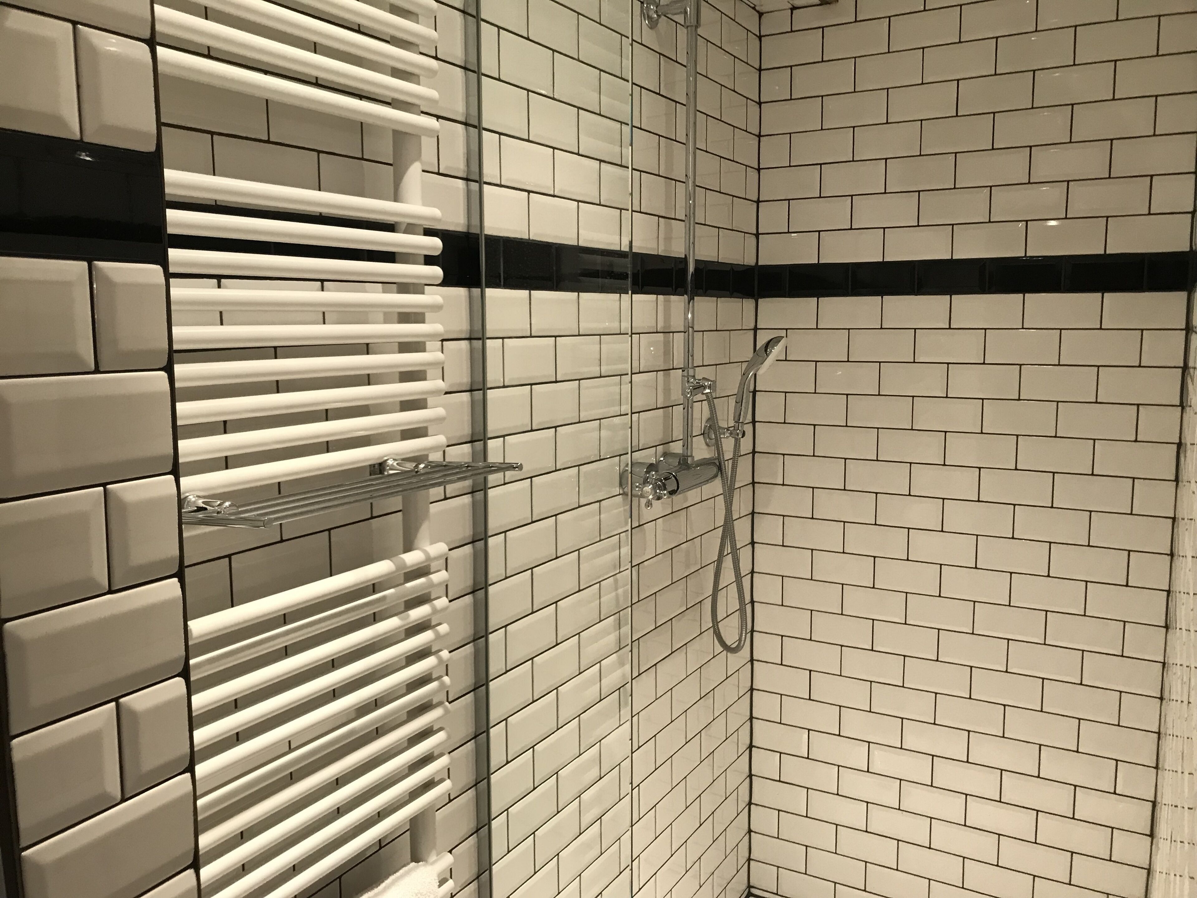 Un espace douche avec des murs recouverts de carreaux blancs et une bande horizontale noire.