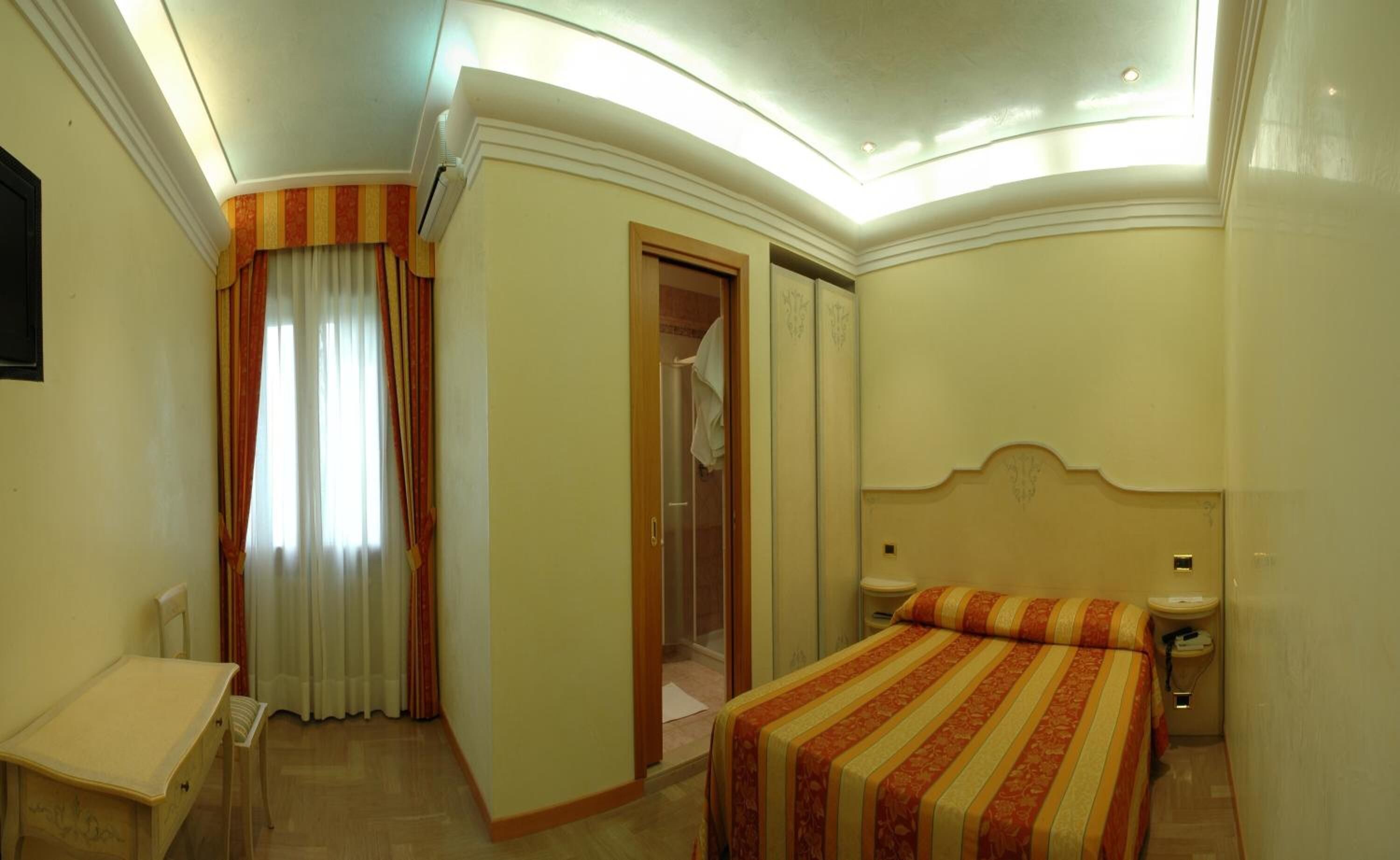 A hotel room with a bed, a bedside table, a nightstand, a wardrobe, and a bathroom.