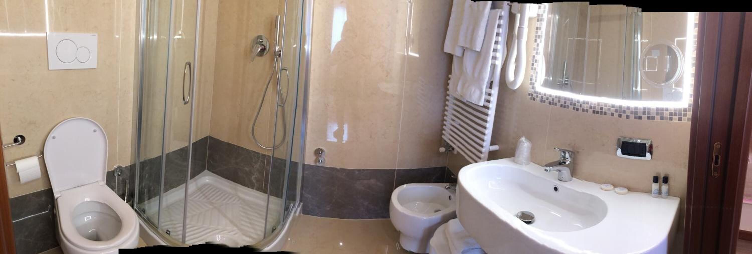 A bathroom with a glass-enclosed shower, a toilet, a bidet, and a sink with toiletries.