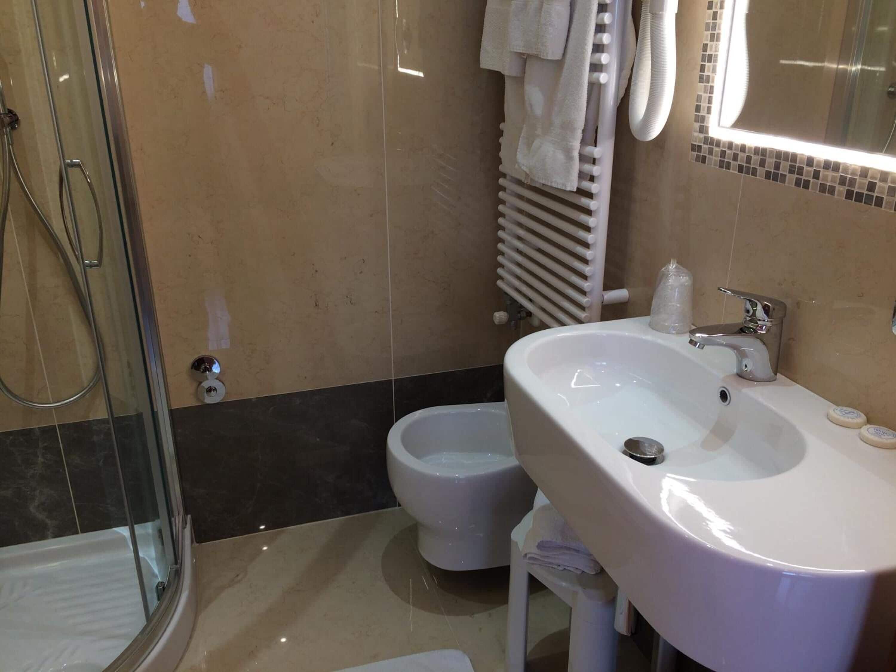 A modern bathroom with a glass-enclosed shower, a bidet, a sink with a mirror, and a towel rack.