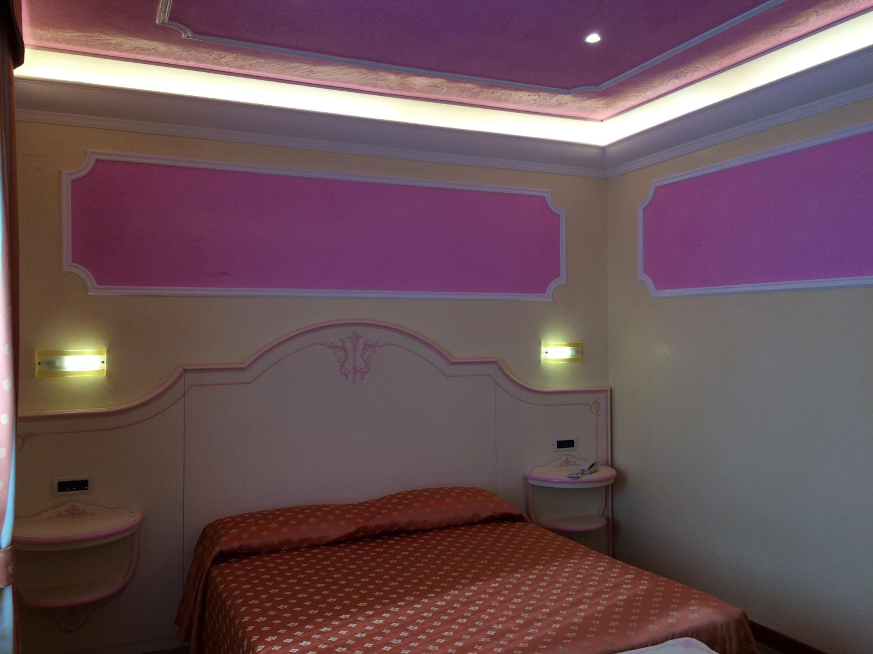 A bedroom with a bed, two bedside tables, and a wall-mounted light fixture.