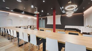 A modern conference room with a long table, white chairs, and a dark ceiling with circular light fixtures.