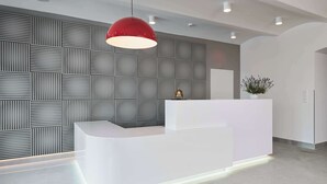 A modern reception desk with a geometric patterned wall and a red pendant light.