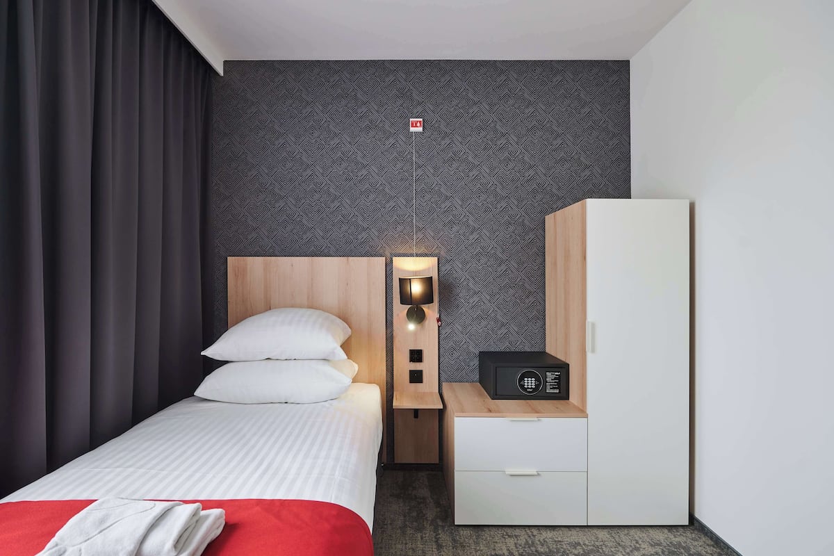 A hotel room with a bed, a bedside table with a lamp, a wardrobe, and a small radio.
