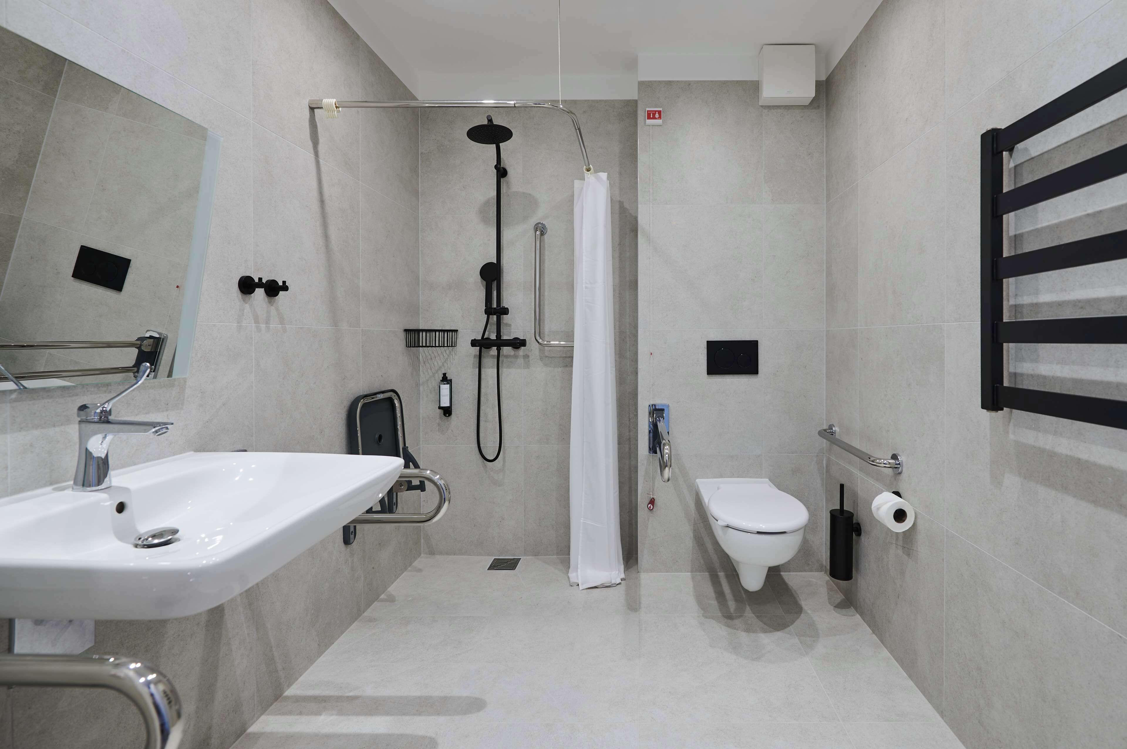 A modern bathroom with a shower, toilet, sink, and handrails.