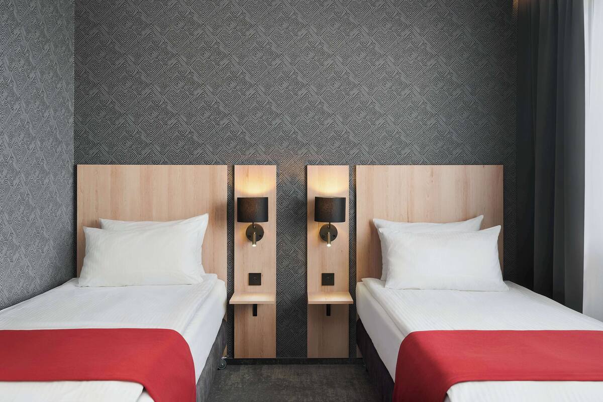 A hotel room with two beds, a patterned wall, and a red accent.