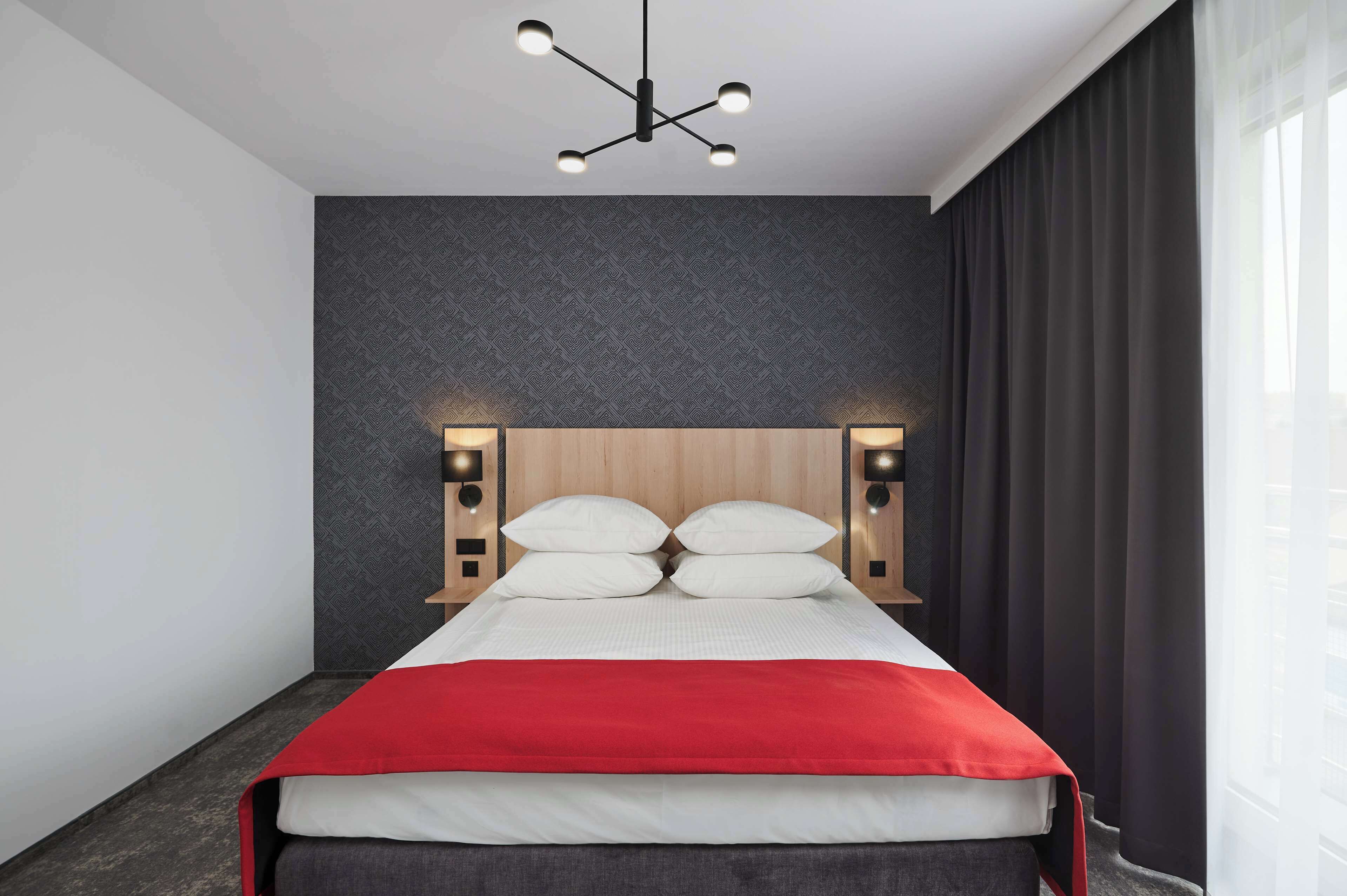 Une chambre d’hôtel moderne avec un grand lit, un mur de couleur sombre et une fenêtre avec des rideaux.