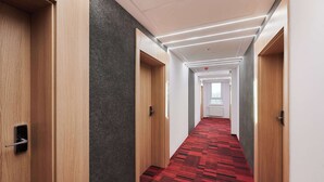 A modern hotel corridor with wooden doors, a red patterned carpet, and recessed lighting.