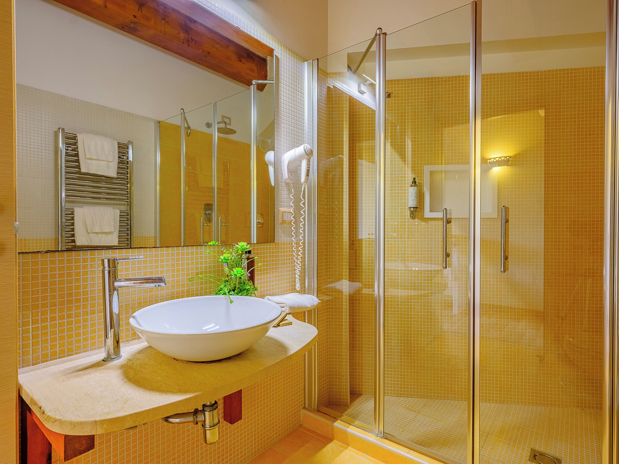 Un baño con un lavamanos grande de color blanco, una cabina de ducha con paredes de vidrio y paredes cubiertas de baldosas amarillas.