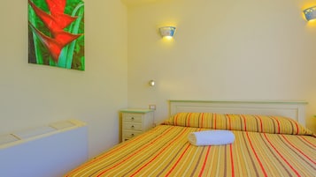 Una cama bien hecha con una colcha a rayas, una obra de arte en la pared con una flor roja, y dos luces en la pared.