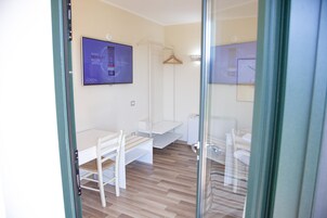 Una stanza moderna e luminosa, con pavimento in legno, una scrivania bianca, una sedia e un attaccapanni.