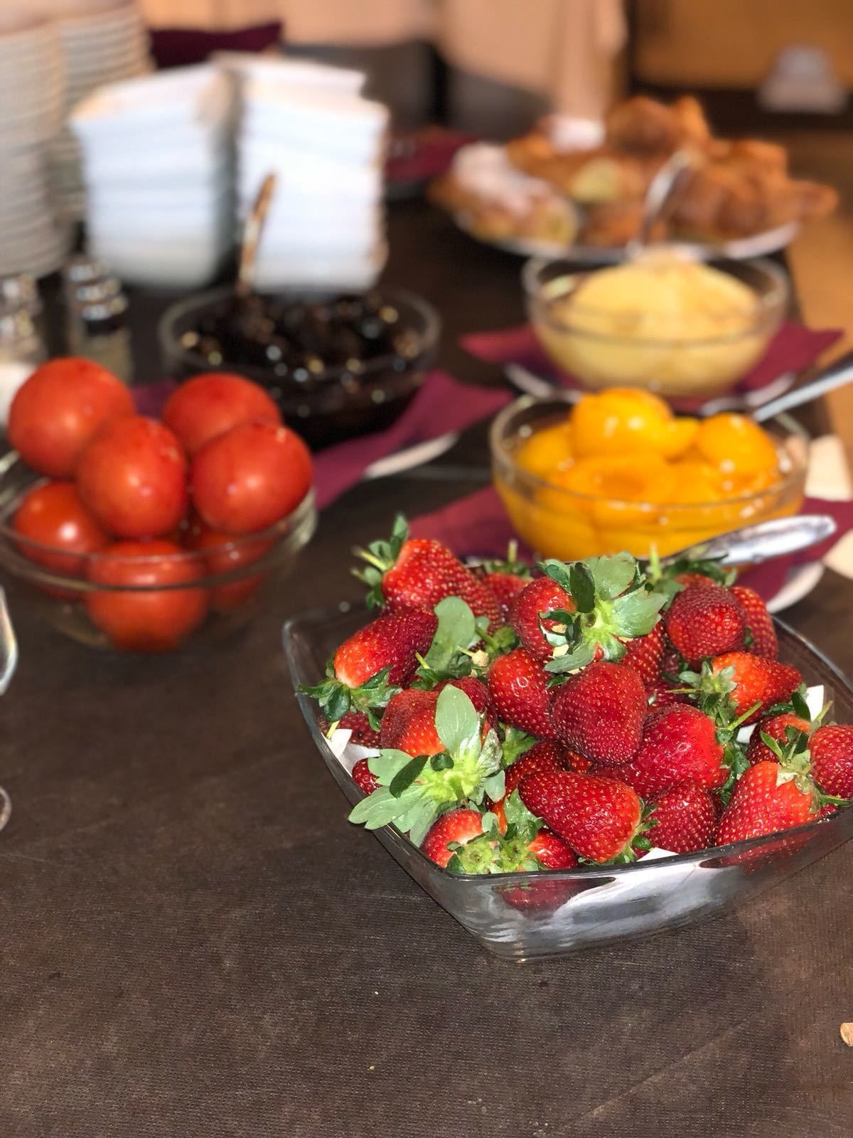A buffet table with various food items including a bowl of strawberries, a bowl of tomatoes, and a bowl of mangoes.