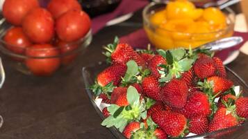 A buffet table with various food items including a bowl of strawberries, a bowl of tomatoes, and a bowl of mangoes.