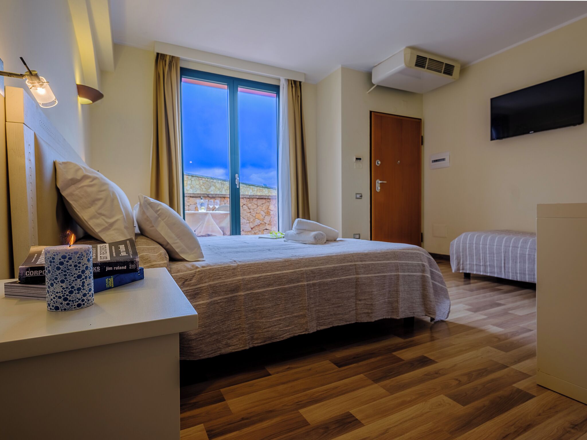Habitación de hotel con cama, mesita de noche, lámpara y televisión en la pared.