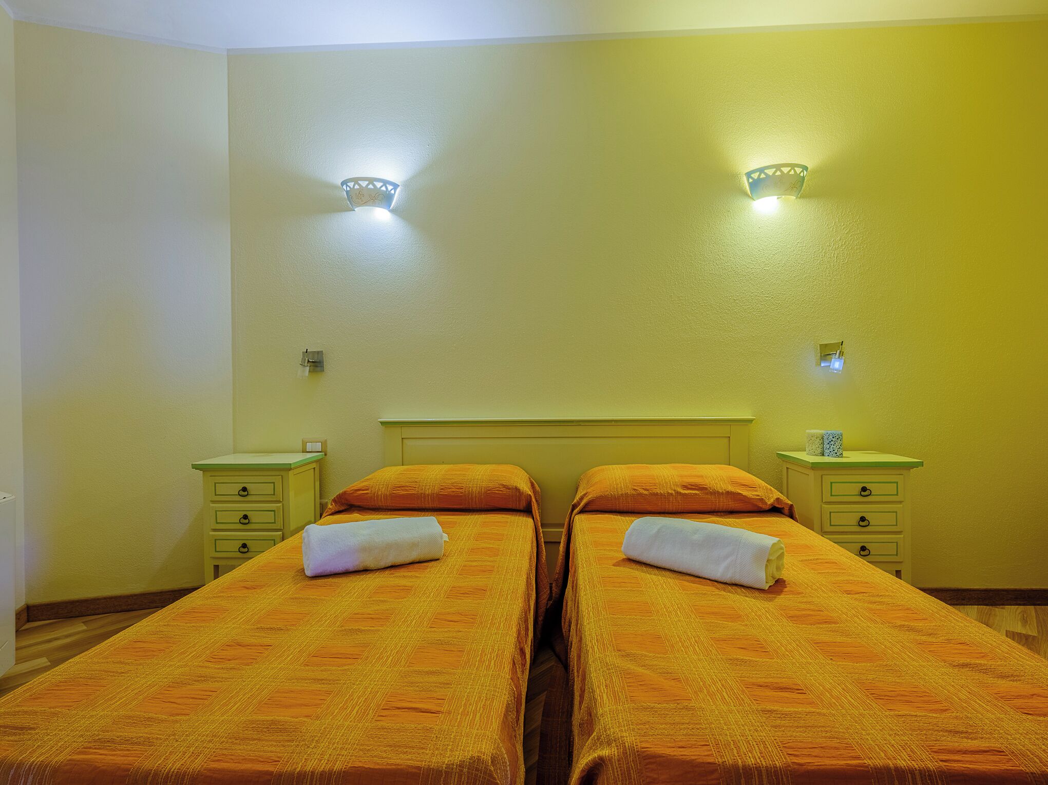 Ein Doppelzimmer mit zwei Betten, jeweils mit orangener Bettdecke und weißen Handtüchern, einem Holzkopfteil und zwei Nachttischen mit Lampen.