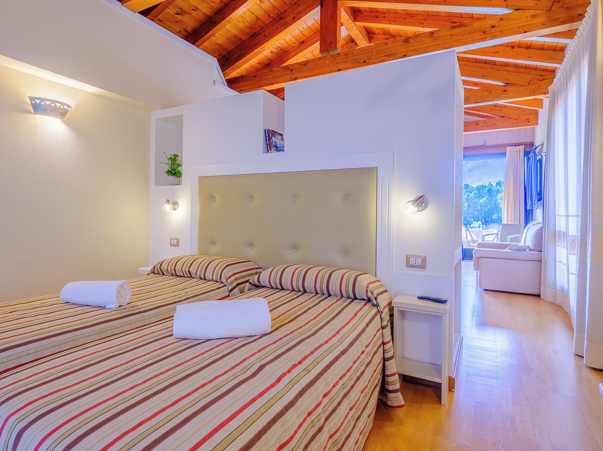 Un dormitorio con dos camas, techo de madera, una mesita de noche y vistas a un balcón.