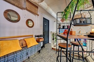 Una habitación acogedora con un sofá a cuadros, un banco de madera, una mesa de comedor con taburetes altos y una planta colgante.