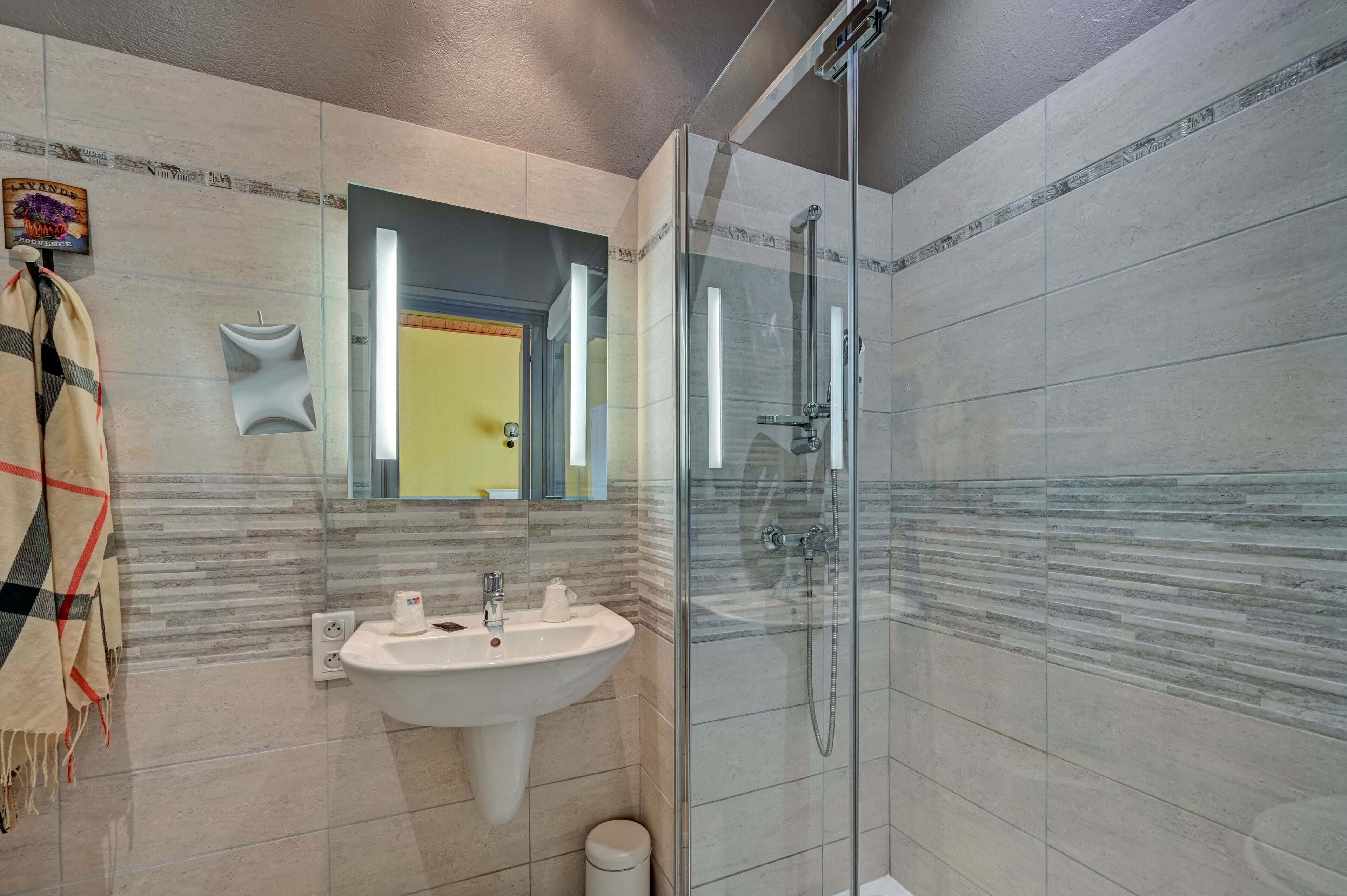 A modern bathroom with a glass-enclosed shower, a sink with a mirror above it, and a towel hanging on the wall.