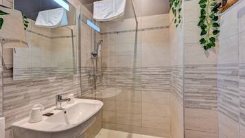 A modern bathroom with a glass shower enclosure, a sink with a mirror, and decorative plants.