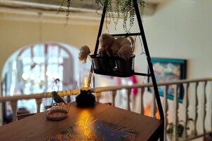 A wooden table with a candle, a decorative mat, and a hanging basket with plush toys.