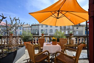 Un espacio al aire libre con sillas de mimbre, una mesa con mantel blanco y una sombrilla naranja que da sombra.