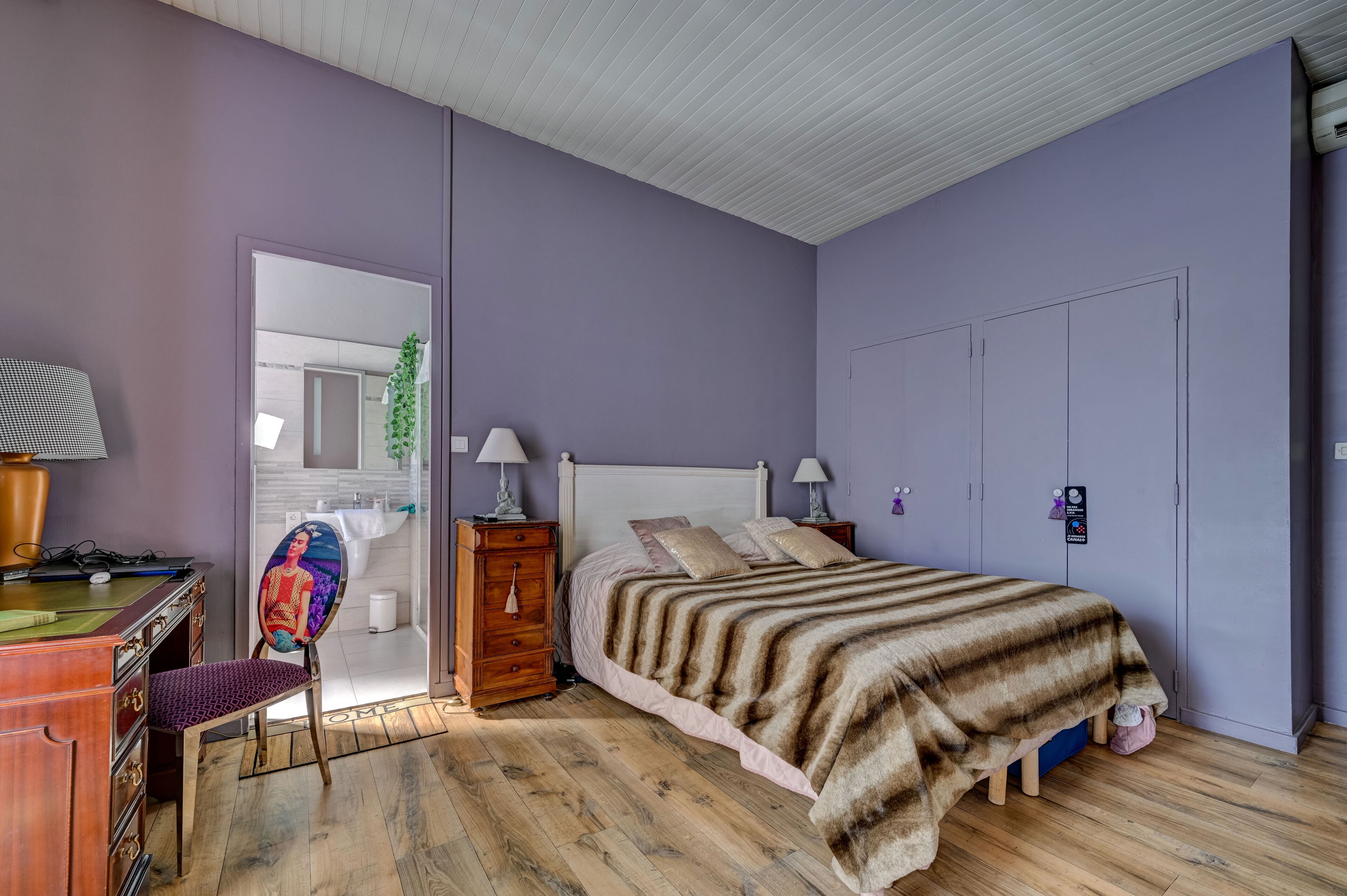 A bedroom with a bed, wooden dresser, chair, bedside tables, and a wardrobe.