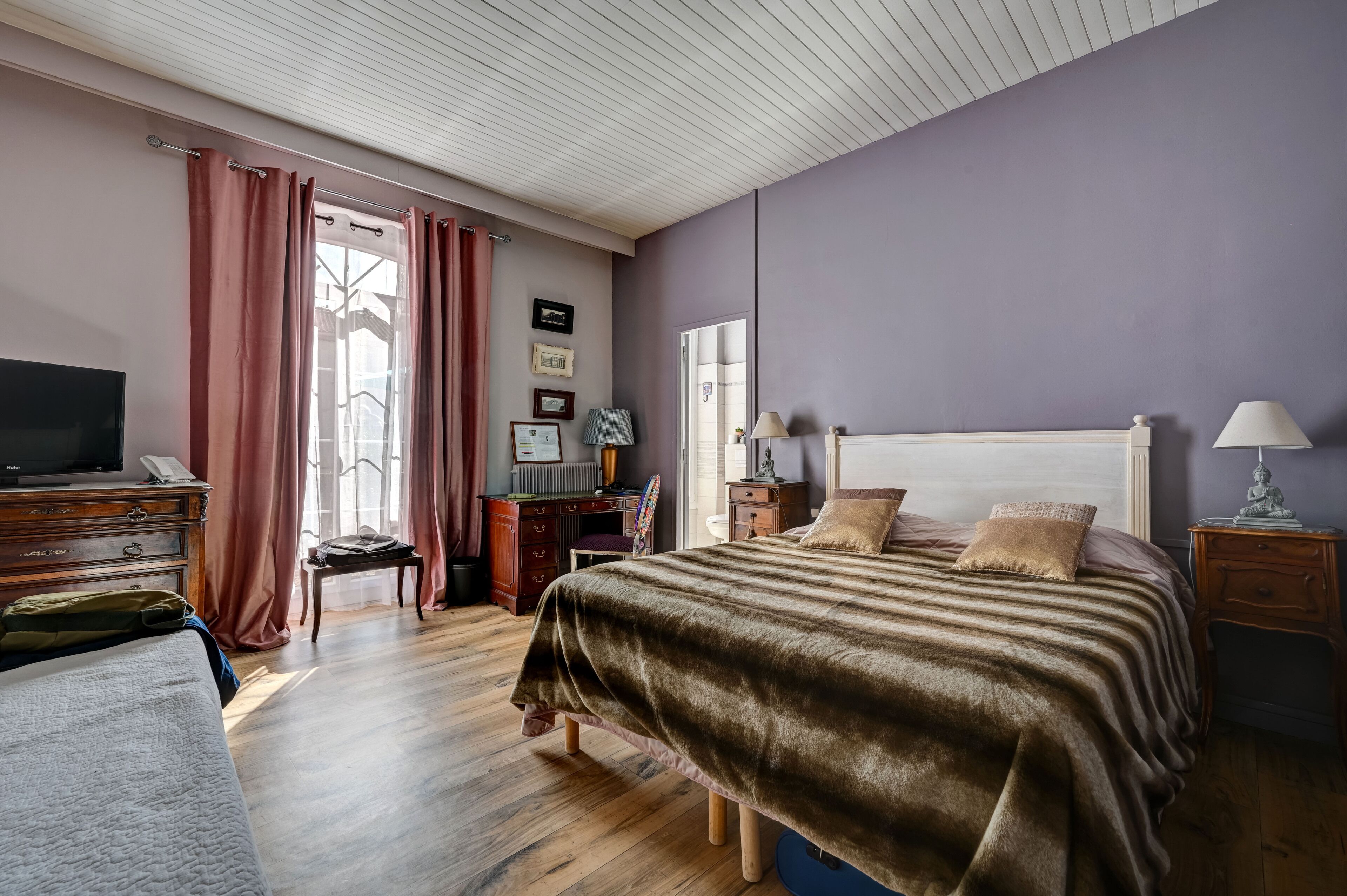 A bedroom with a bed, bedside tables, a desk, a chair, and a television.