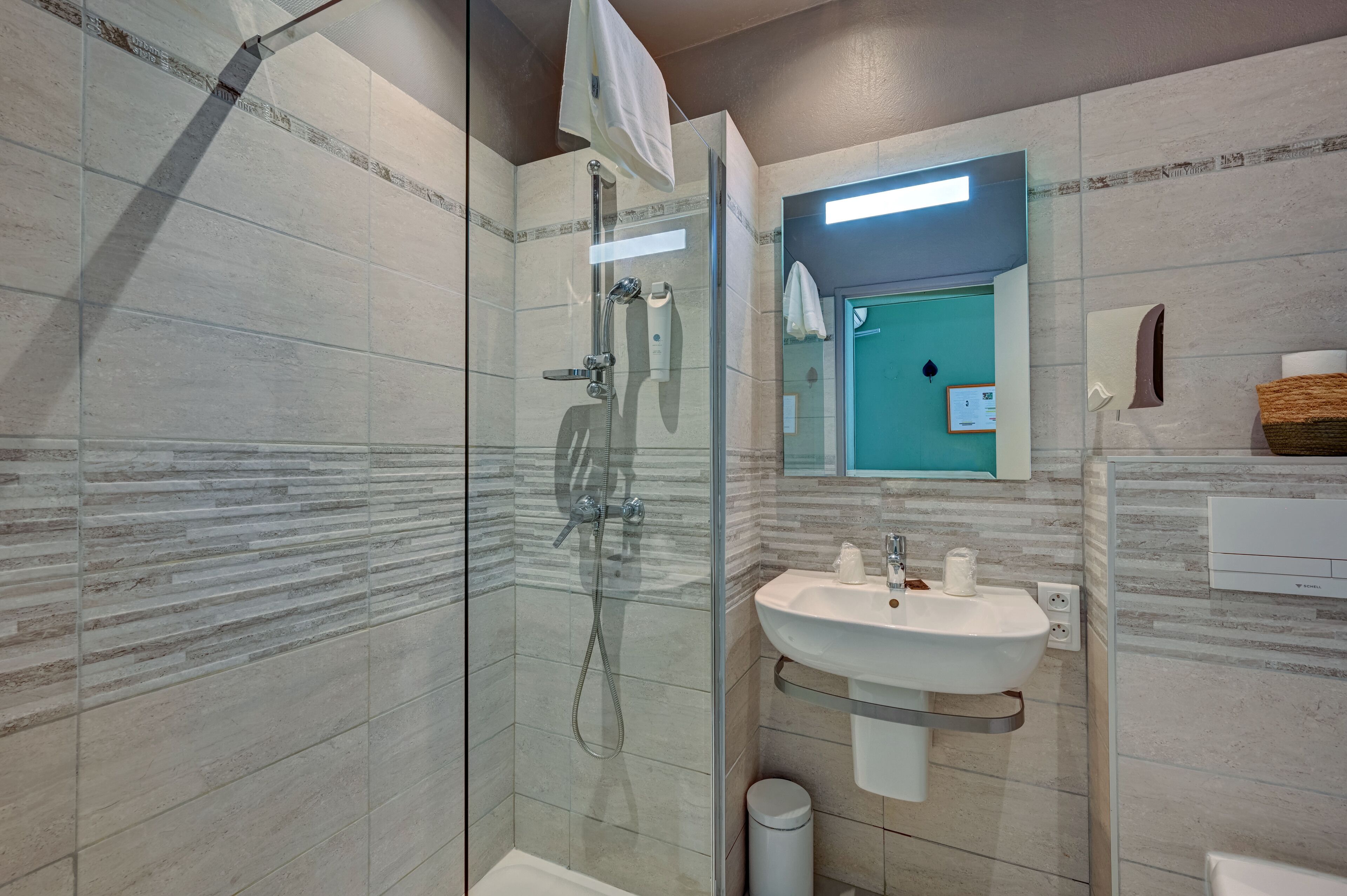A modern bathroom with a glass shower enclosure, a sink with a mirror, and a towel hanging on the wall.