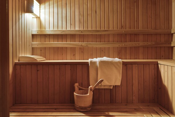 A wooden sauna with benches, a towel, and a wooden bucket.