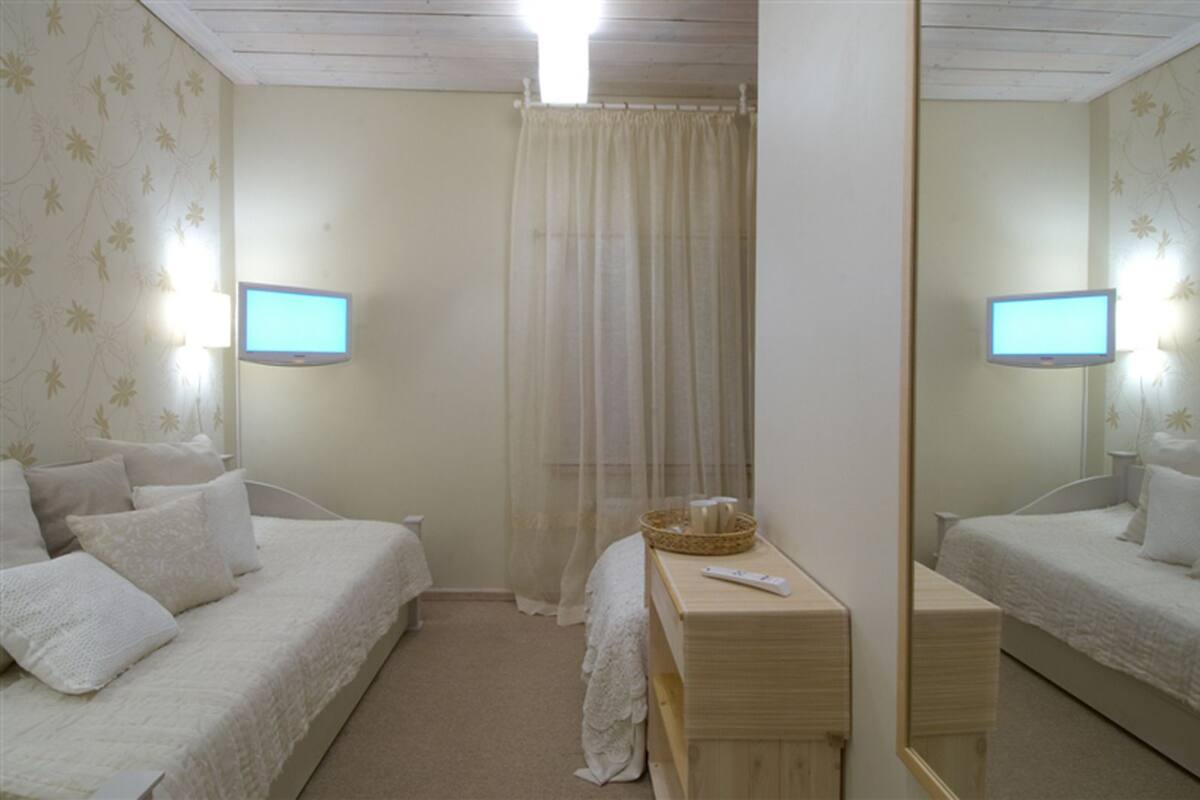 Un dormitorio con dos camas, una mesita de noche, un espejo y una ventana con cortina translúcida.