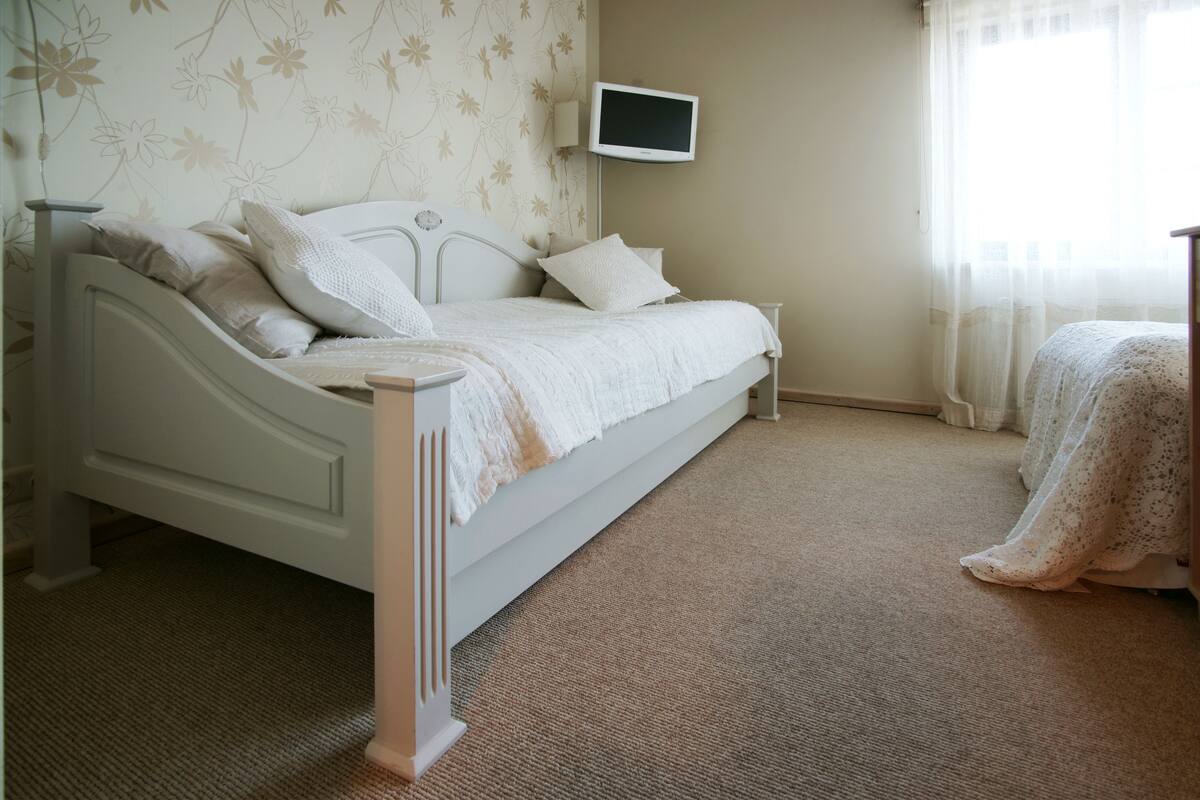Un dormitorio con una cama, un televisor montado en la pared y una ventana con cortinas.