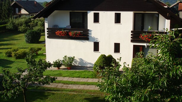 A two-story house with a balcony, surrounded by greenery and mountains in the background. - Apartmaji Vidic- Guest House (Bled)