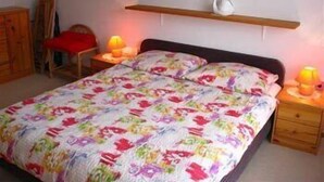 A bedroom with a bed, two bedside tables, a nightstand, a wooden dresser, and a wall-mounted shelf with a lamp. - Apartmaji Vidic- Guest House (Bled)