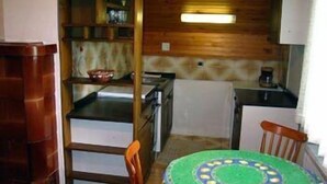 A compact kitchen with wooden cabinets, a small refrigerator, and a round table with a green and blue pattern. - Apartmaji Vidic- Guest House (Bled)