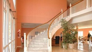Eine geräumige Lobby mit Marmorboden, einer geschwungenen Treppe mit weißen Geländern und einer großen Topfpflanze.