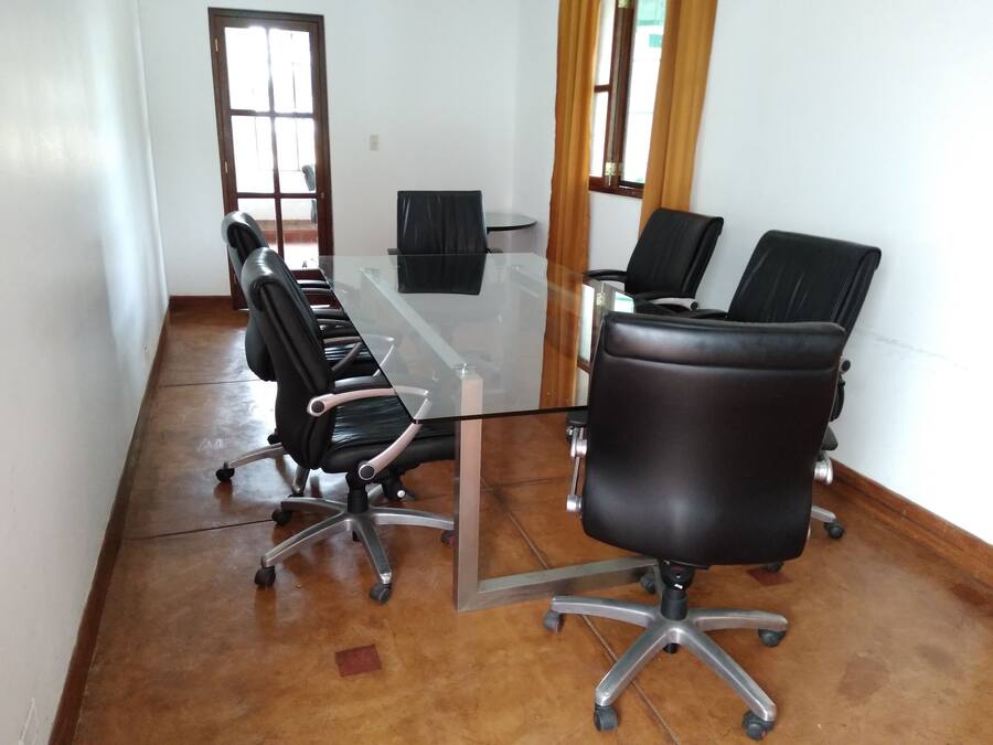 A conference room with a glass table, black office chairs, and a wooden floor.