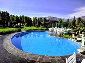 A swimming pool with lounge chairs and umbrellas, surrounded by greenery and mountains in the background. - Casa Hacienda Nasca Oasis (Nazca)
