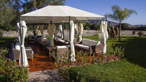 An outdoor patio with wicker furniture and a canopy, surrounded by greenery and flowers. - Casa Hacienda Nasca Oasis (Nazca)